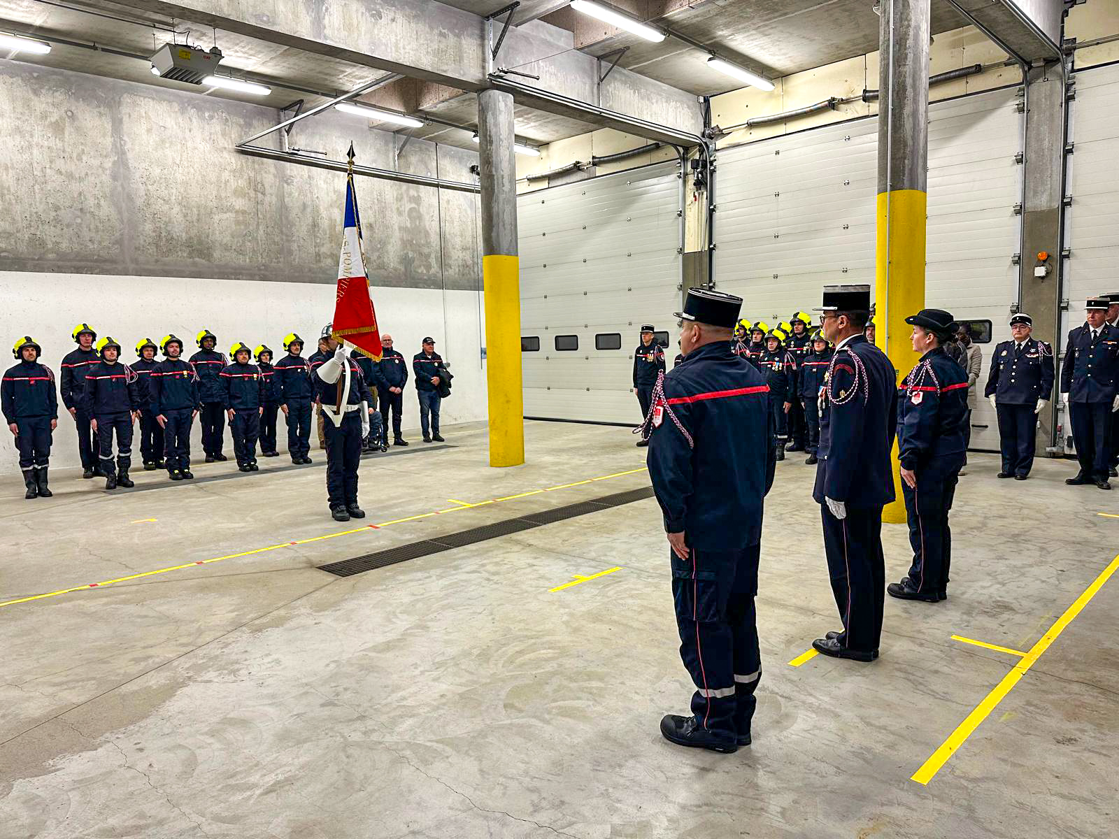Un groupe de pompiers en uniforme se tient debout dans une grande salle, affichant une posture solennelle et organisée.